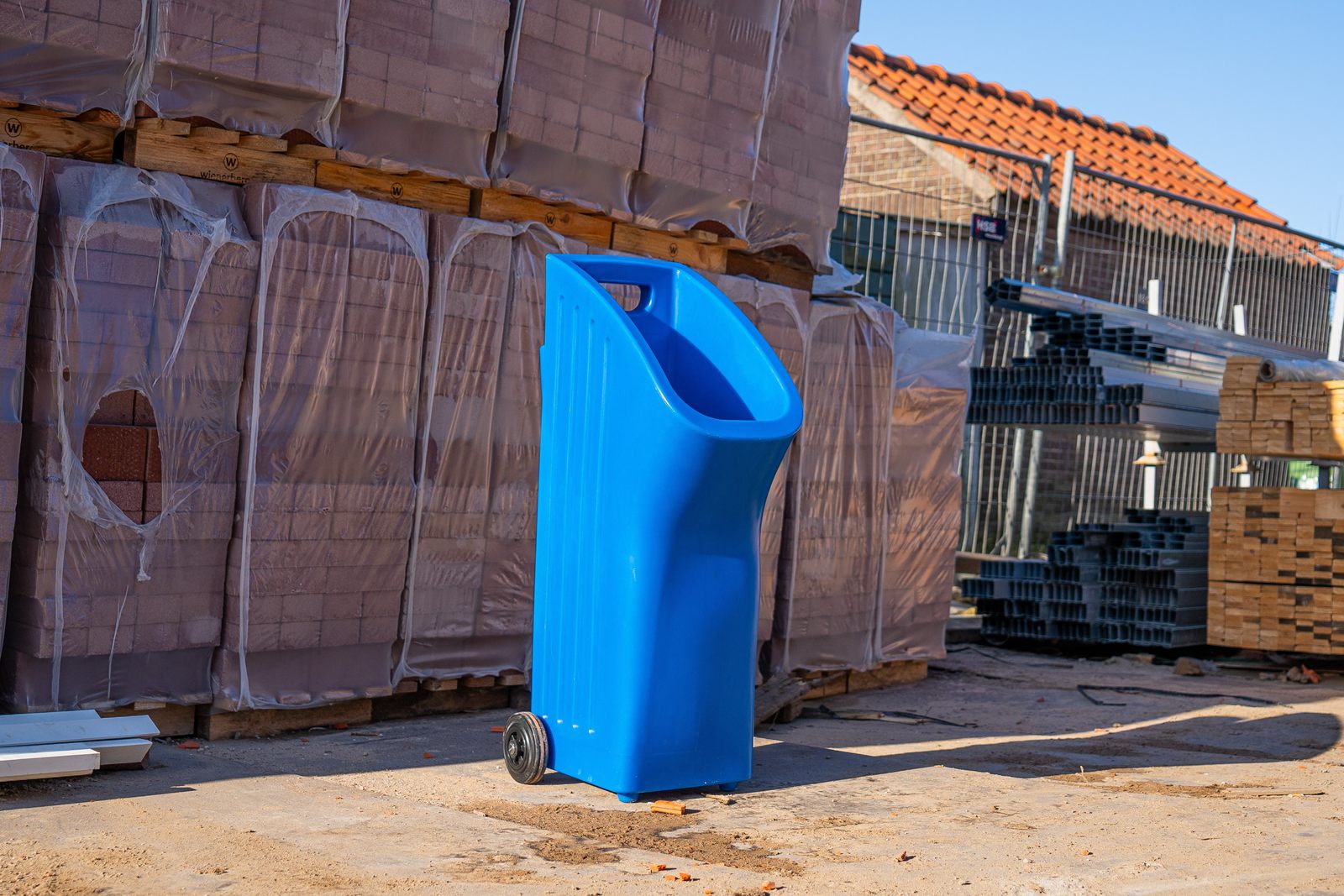 Het blauwe Easy Peezy urinoir op een bouwplaats, naast pallets met bakstenen.